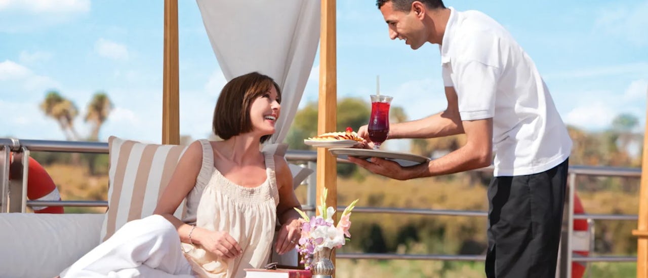 Gast auf einer Sonnenliege beim Erhalten eines Getränkes auf dem Kreuzfahrtschiff River Tosca